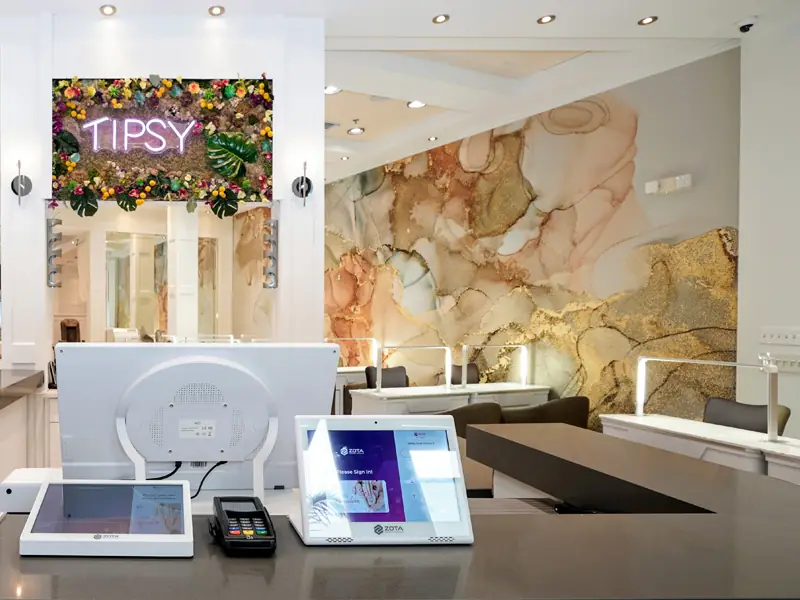 The front desk, with a pink neon Tipsy sign set into a floral wall