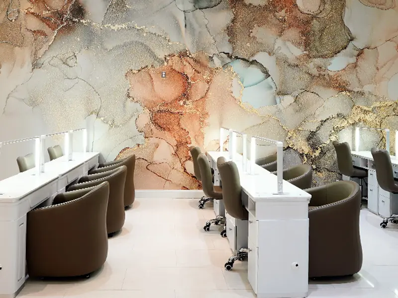 A wide view of the manicure floor at Tipsy Nails & Spa, stations along the blush and gold mural wall